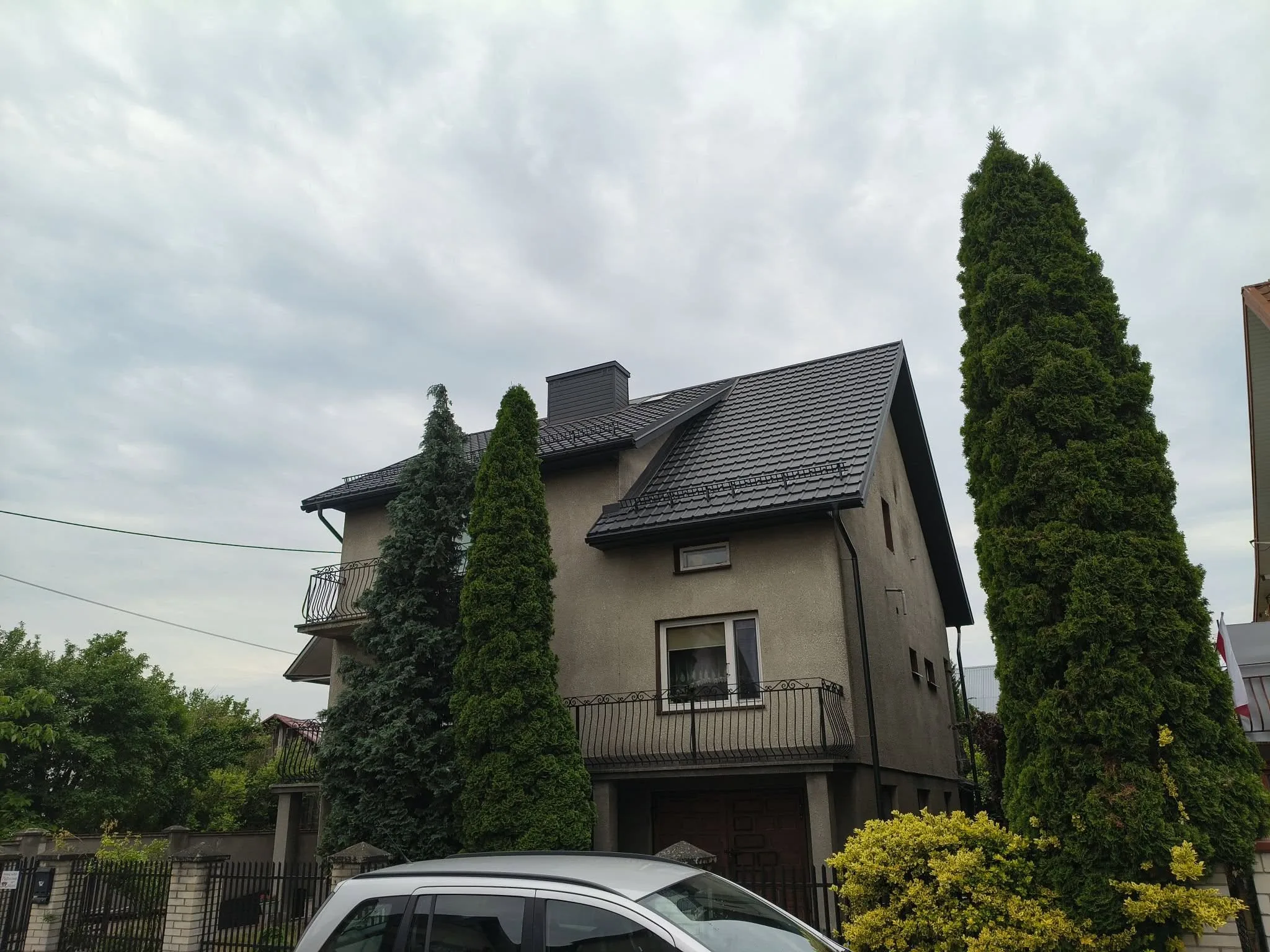 Dom piętrowy z ciemnym dachem krytym dachówką